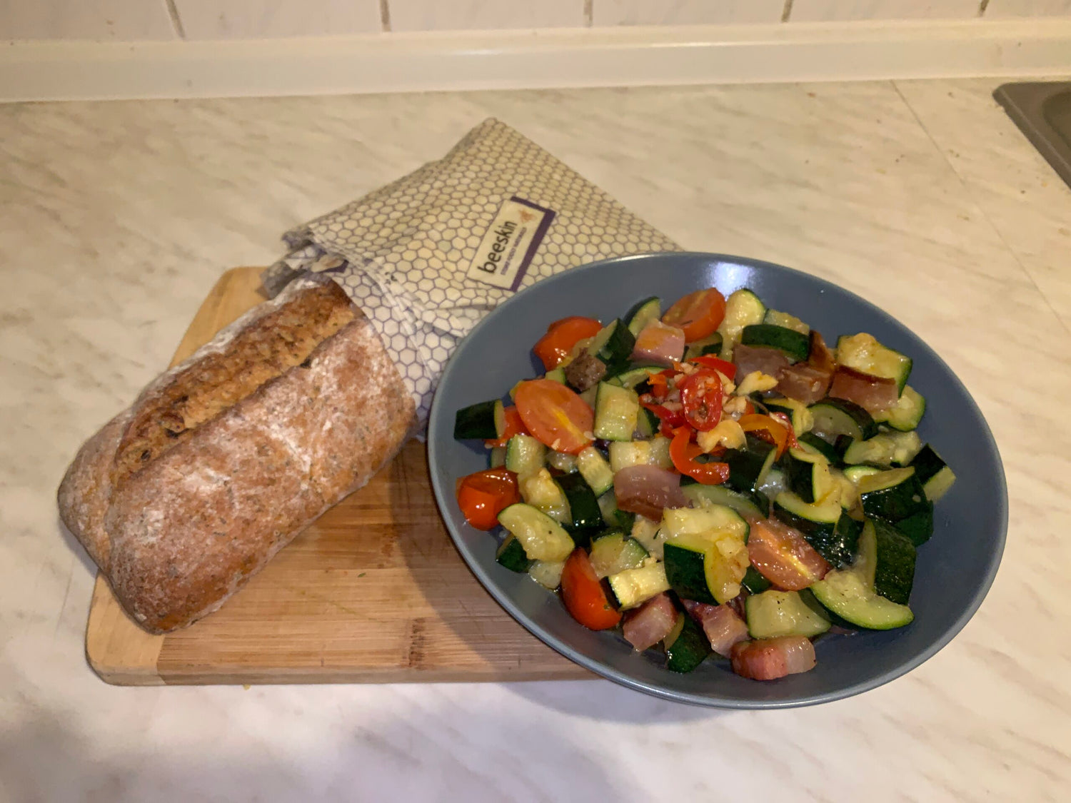 photo showing a bread load wrapped in beeskin beeswax wraps size XL in standard design and a plate with cooked zucchini bruschetta