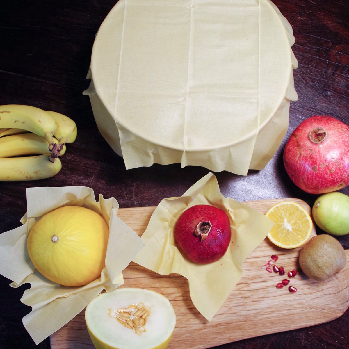 beeskin beeswax wrap multi natural on a bowl and pomegranate and melon on a beeswax rap next to different fruit