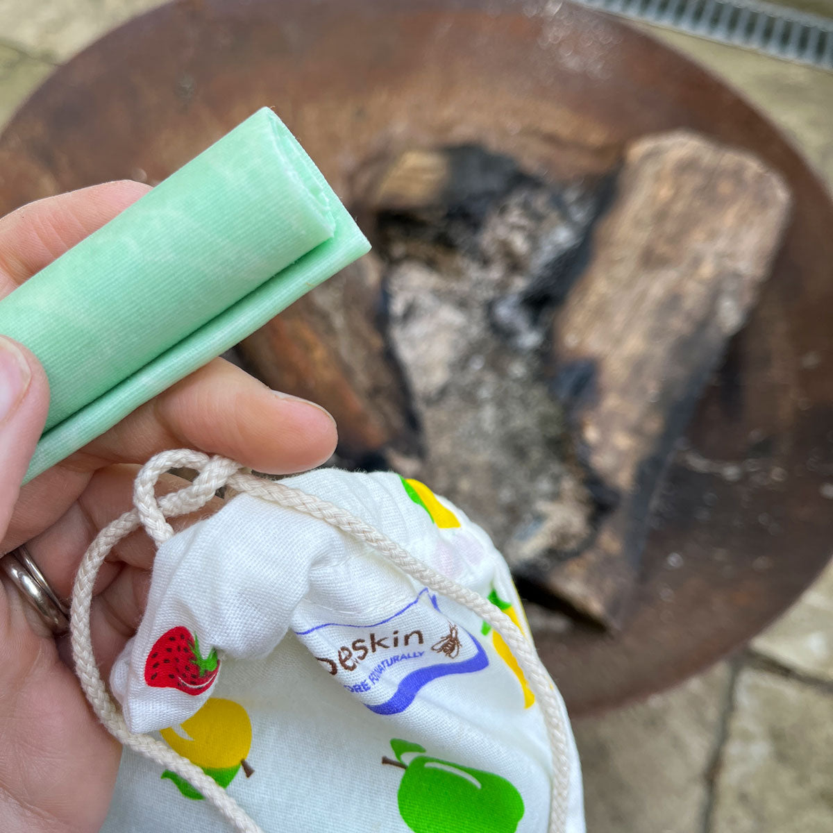 hand holding firestarter and a fabric bag in front of a campfire