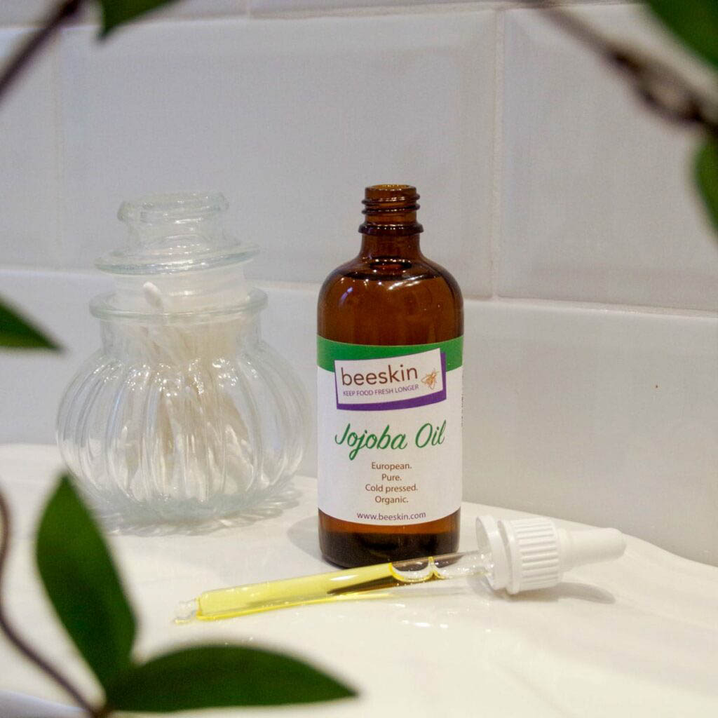 Pipette filled with Jojoba Oil lying next to the open bottle in a bathroom