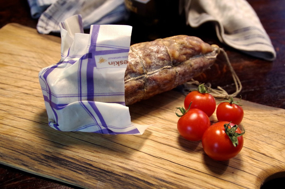 sliced salami wrapped in beeskinbeeswax wrap s kitchen on a wooden board with tomatoes