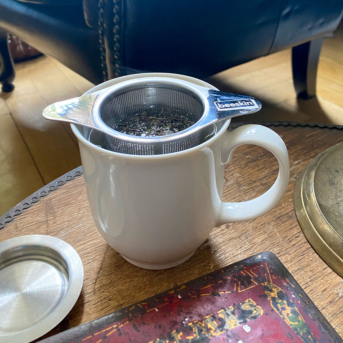beeskin tea infuser filled with tea inside a white porcelain mug with hot water standing on a table