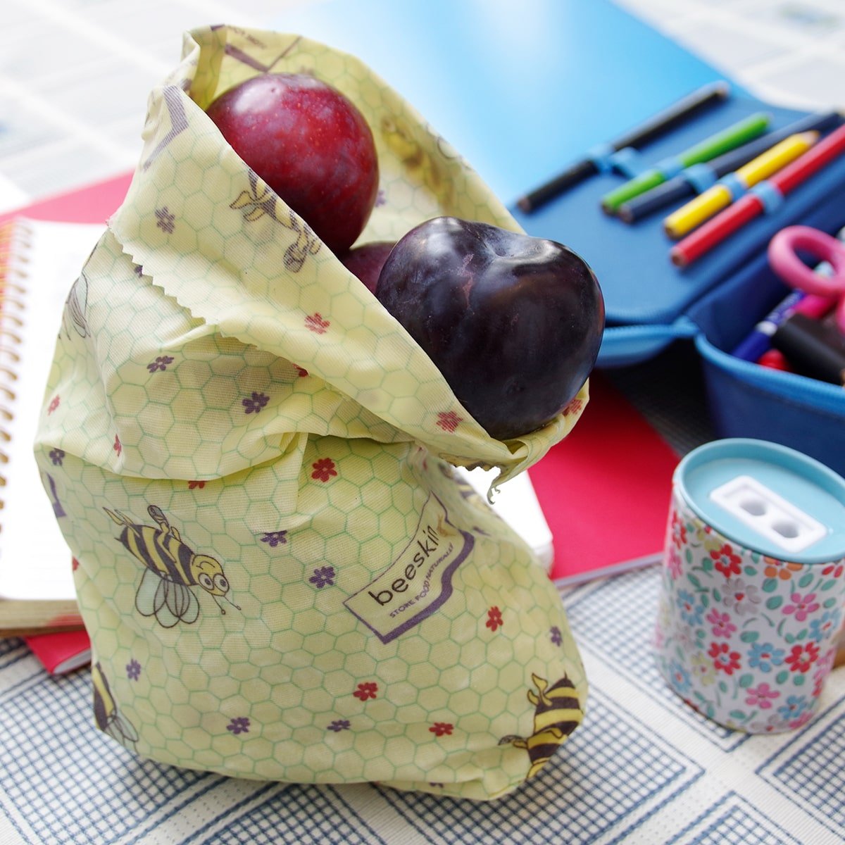 beeswax bag size s standing on a table with plums in it surrounded by paper and pens