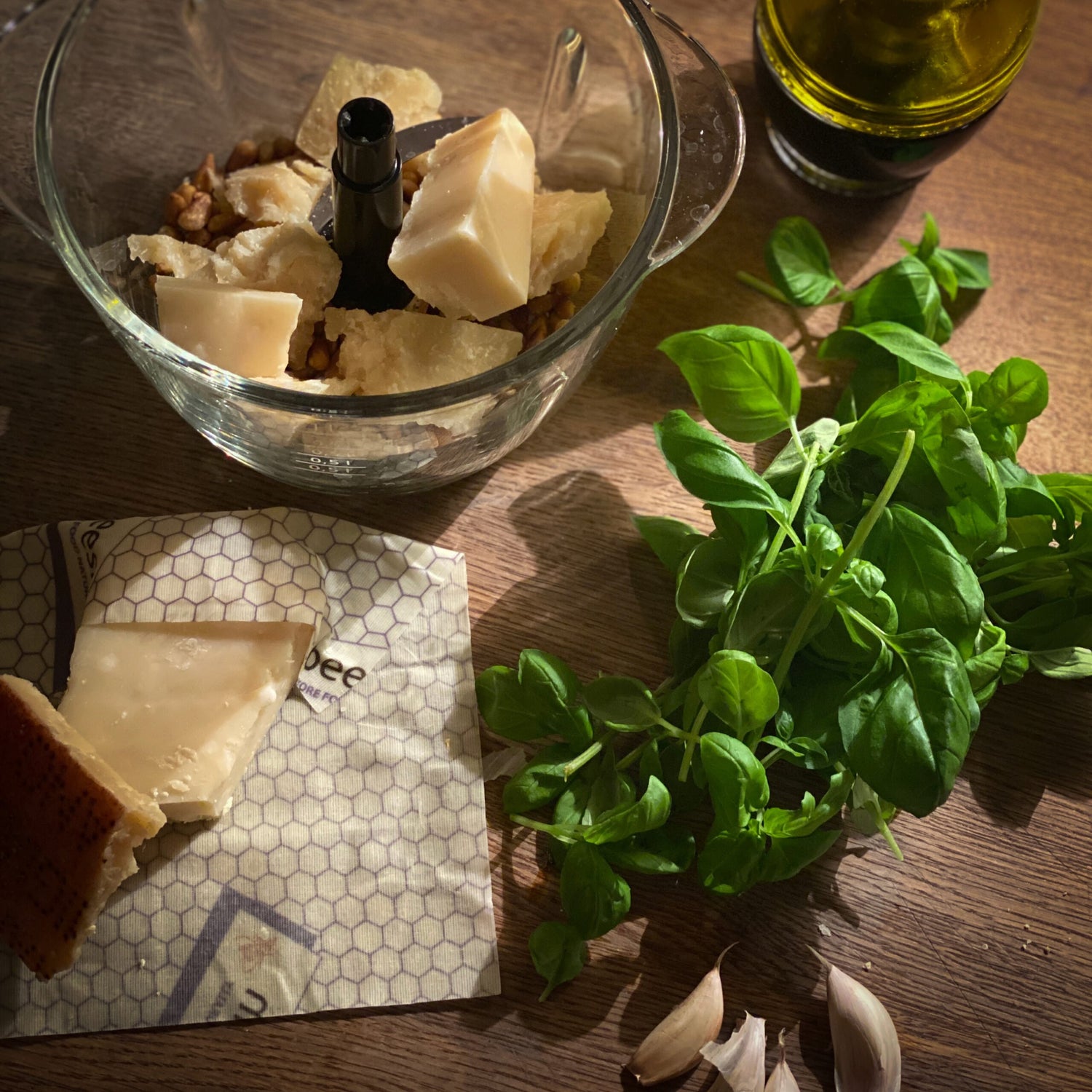photo showing olive oil bottle, basil, cubed parmesan cheese, and a triangle of parmesan cheese wrapped in beeskin beeswax wraps size L in standard design