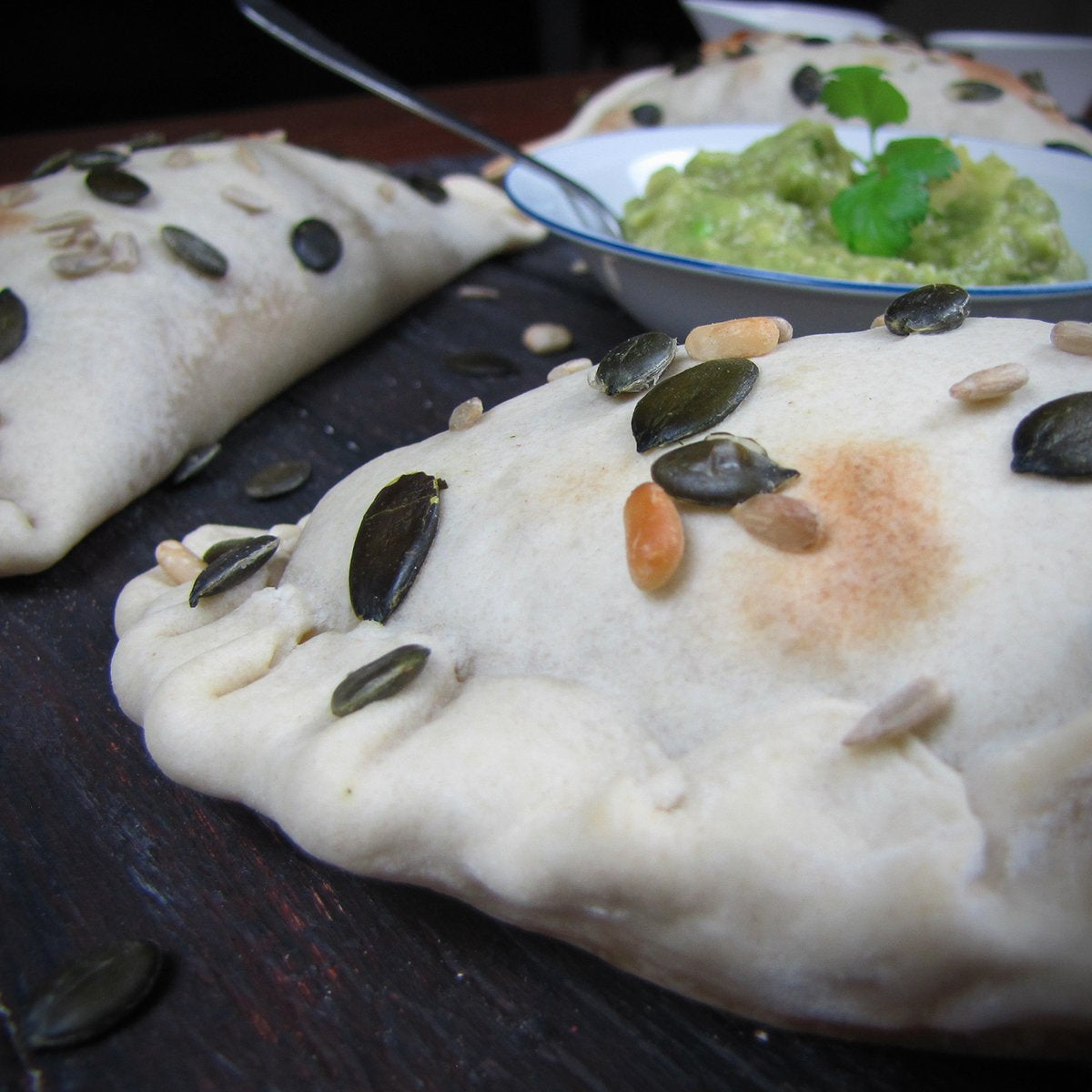 photo showing closeup of cooked empanada with avocado salsa and pumpkin seeds