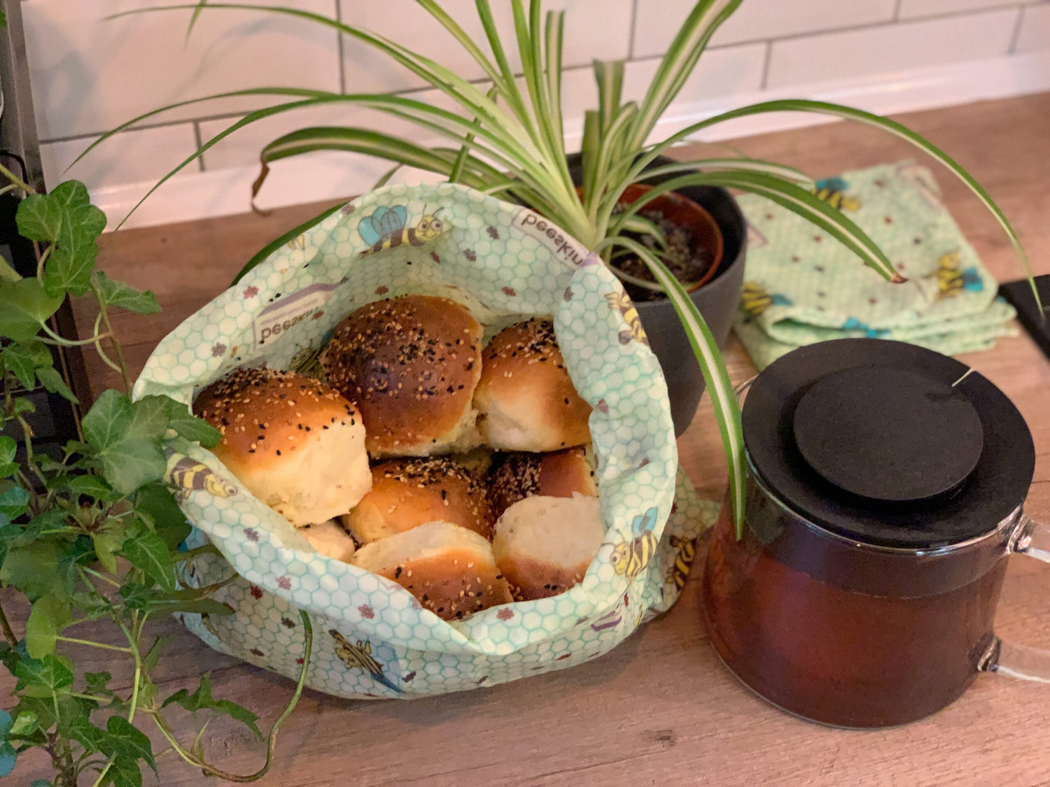 photo showing bread buns in beeskin beeswax Bag L in kids design alongside teapot and a plant