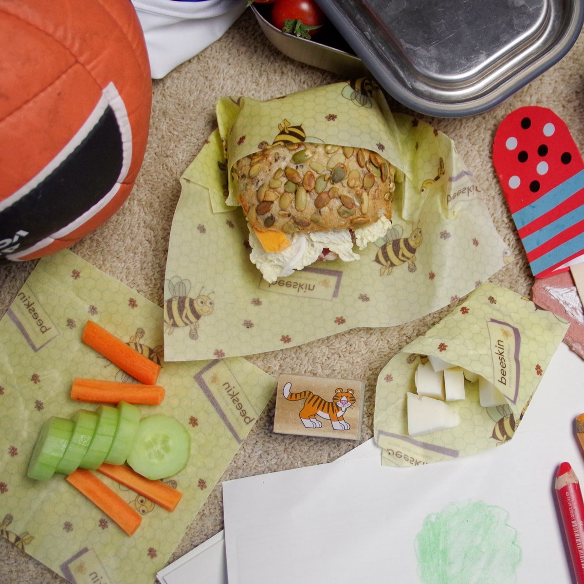 beeskin beeswax wrap kids set wrapping food such as roll, carrots, cheese on a table full of school supplies