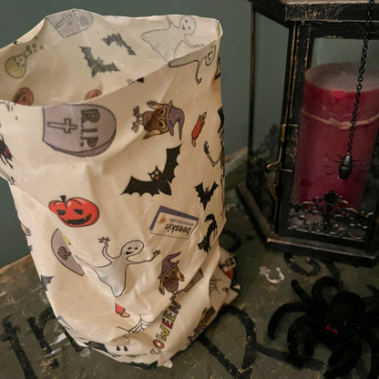 beeswax bag halloween showing ghosts, pumpkins, bats, black cats and logo beeskin standing next to a red candle