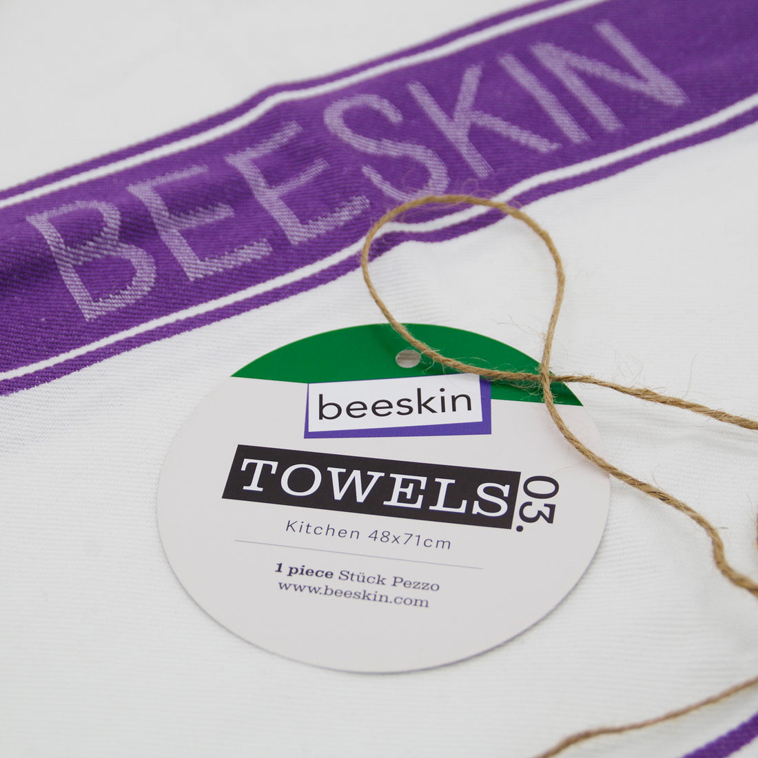 unfolded tea towel white/purple with beeskin logo, the tag lies on it