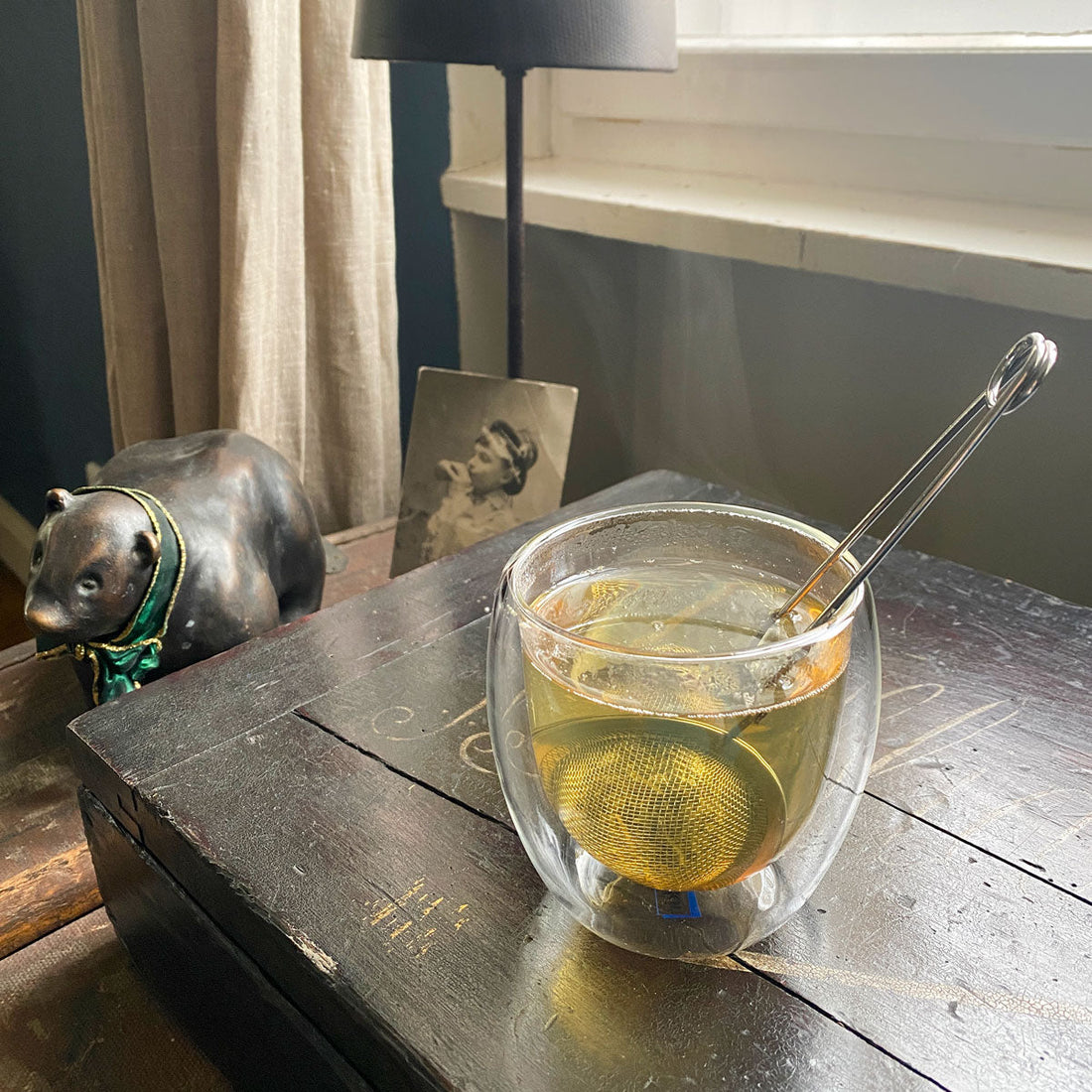 small tea infuser filled with tea in a double walled glass standing on a wooden box