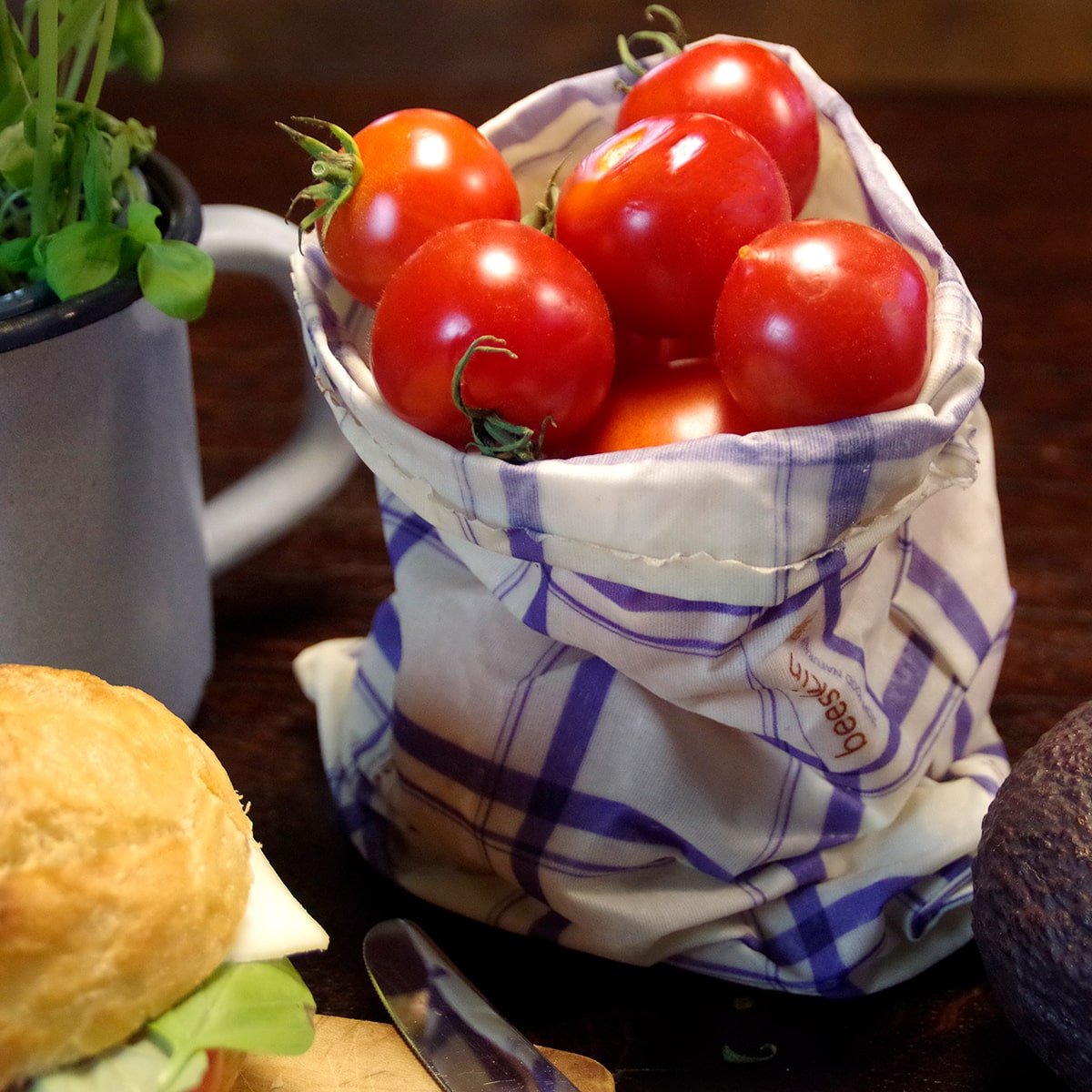 beeswax bag size s kitchen standing on a wooden table with tomatoes surrounded by a roll and an avocado