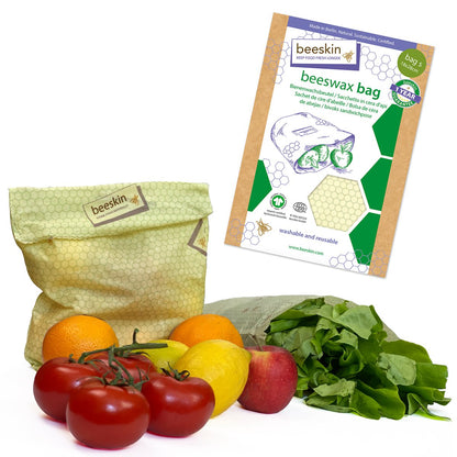 beeskin beeswax wraps bag in size s. Multilingual packaging with window and color coded size indication. Shown with different produce in front of packaging. tomatoes, lemons, lettuce and oranges.