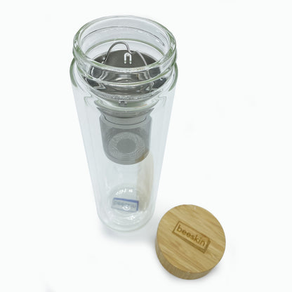 glass tea bottle open with tea strainer and wooden lid with beeskin logo besides