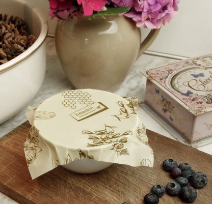 beeskin beeswax wrap flower unpacked covering a little bowl next to blueberries and pink flowers